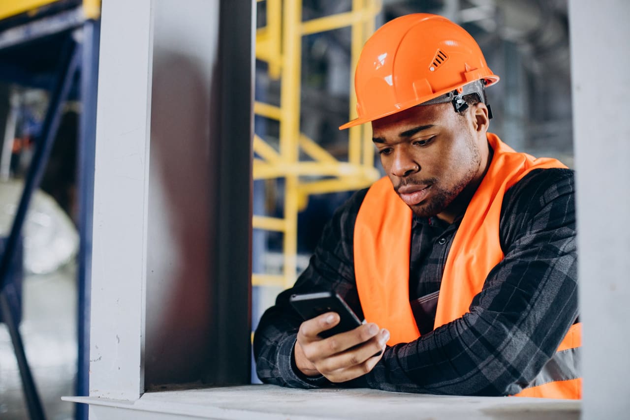 An engineer in a hard hat reads a job on his phone